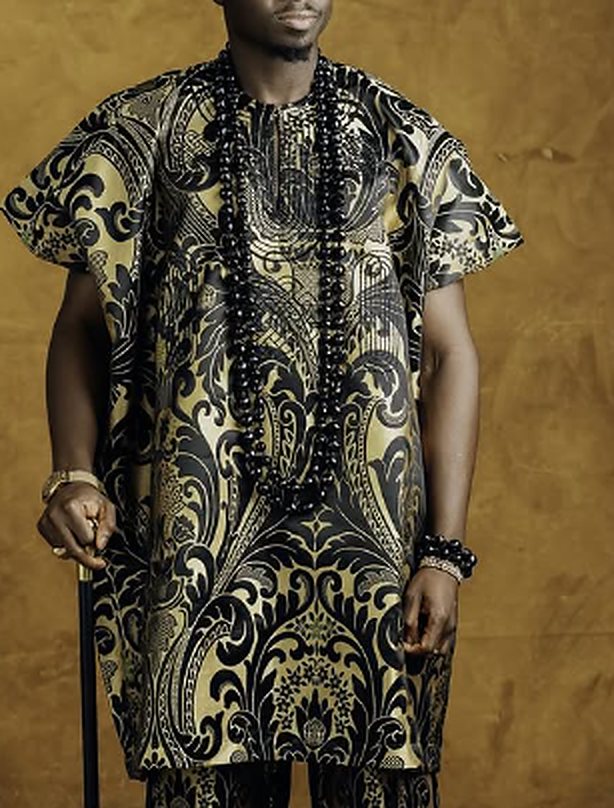 Model wearing a black and gold damask brocade wide-sleeve top with matching trousers and long black bead necklaces