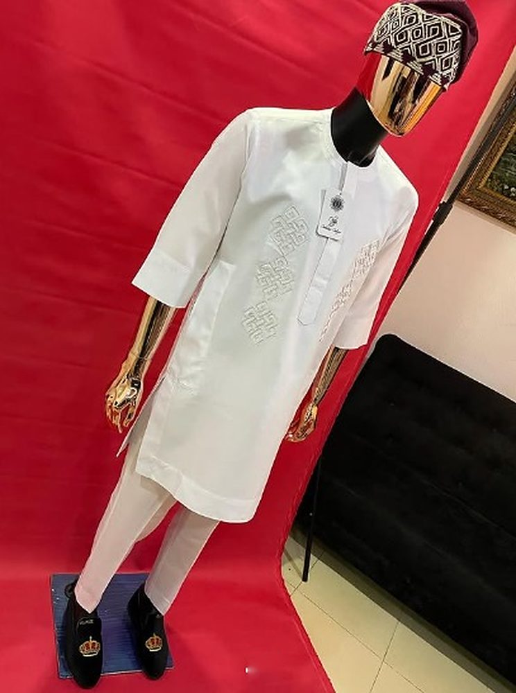 Ivory senator with tone-on-tone endless-knot embroidery and matching trousers on a mannequin against a red backdrop